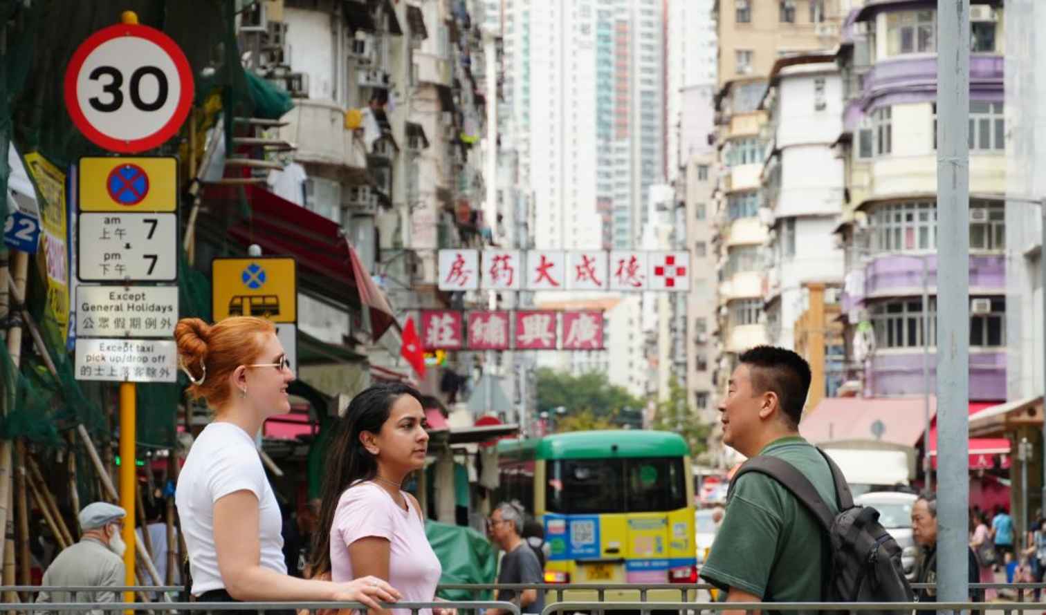 Three people stand on a busy street in Hong Kong.