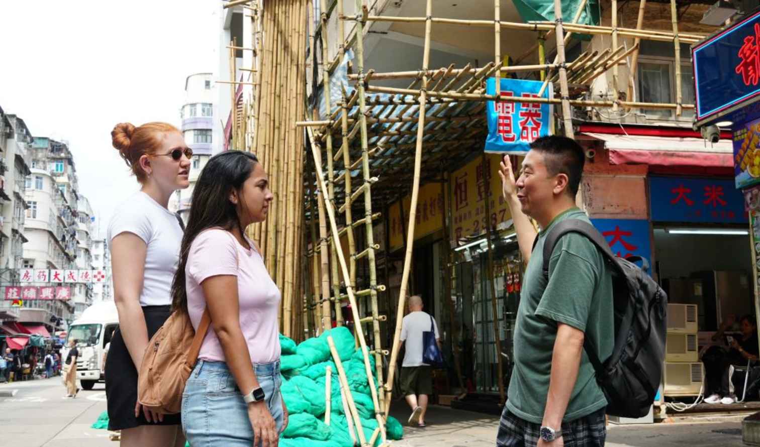 Two women and a man discuss in a Hong Kong street.