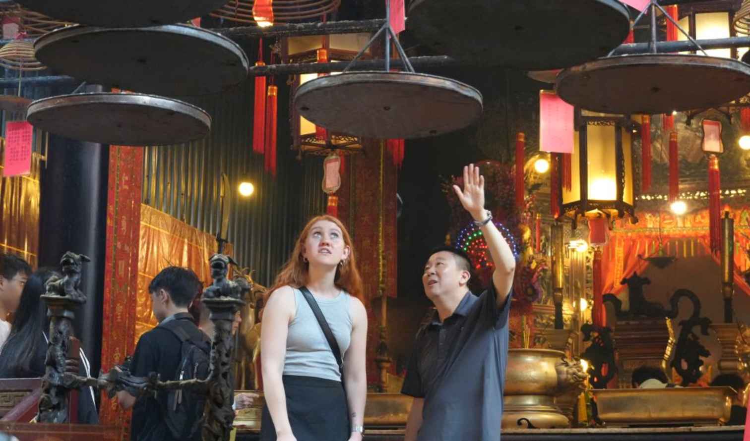 Two people inside Man Mo Temple, Hong Kong, looking at hanging incense coils.