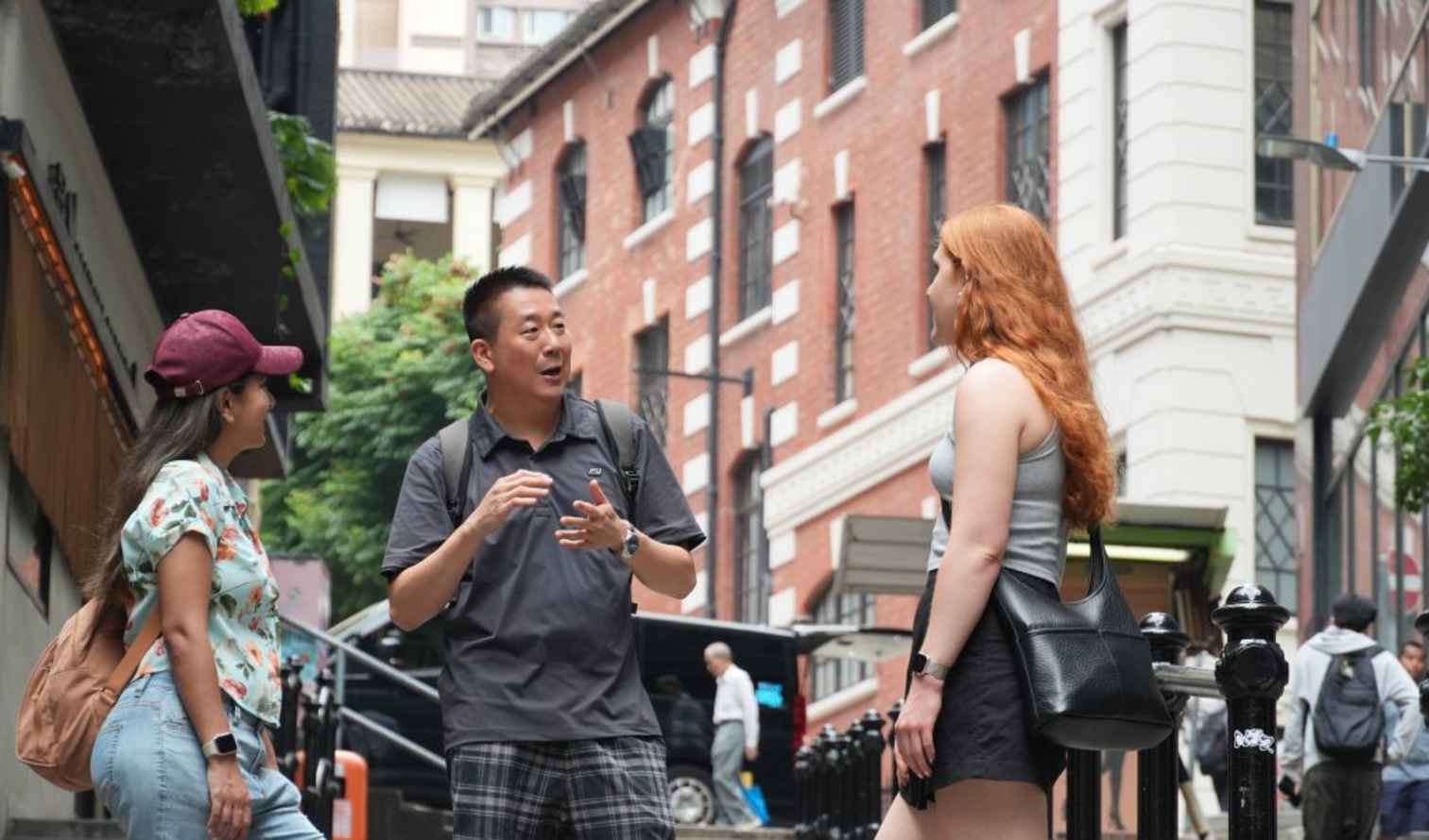 Three people talking on a city street with red brick buildings in Hong Kong 