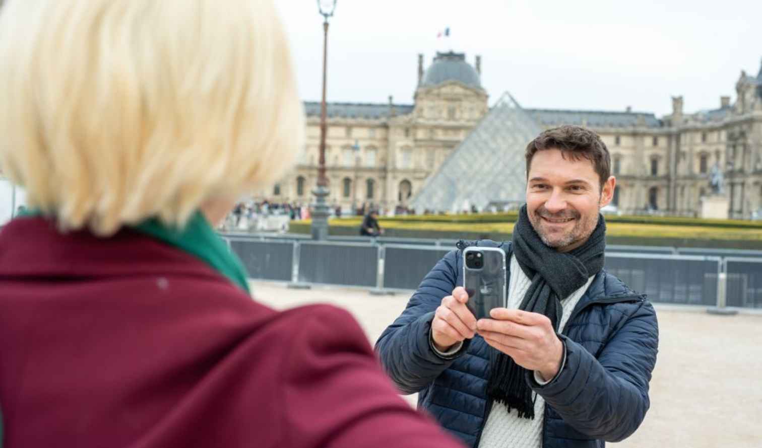 A person taking a photo near the Louvre Pyramid in Paris.