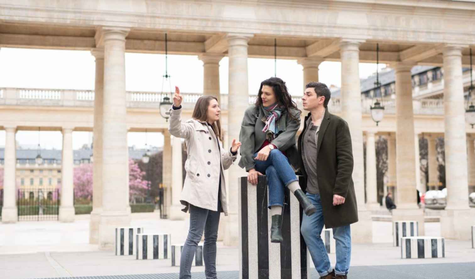 Three people interact at Palais Royal in Paris, with columns in the background.