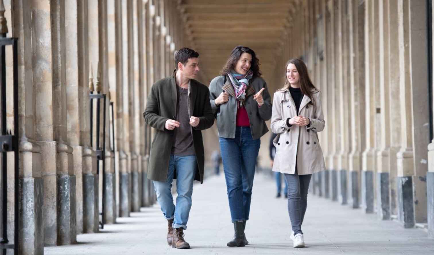 Three people walking under the arches of Palais-Royal in Paris.