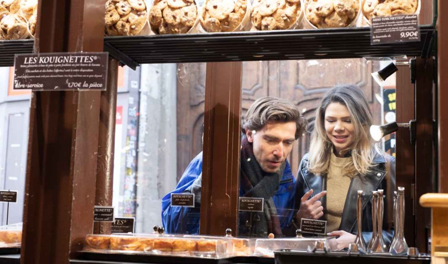 Bakery window display with pastries labeled 'Les Kouignettes' in Paris.