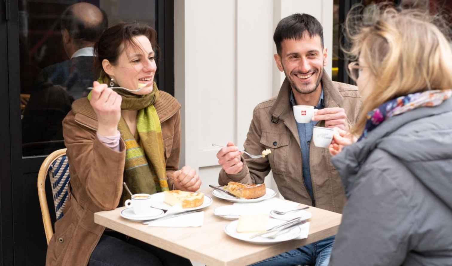 Three people having coffee and dessert at an outdoor café table in Paris.