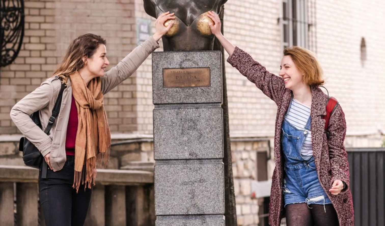 Two people touching a bust at Place Dalida in Montmartre, Paris.