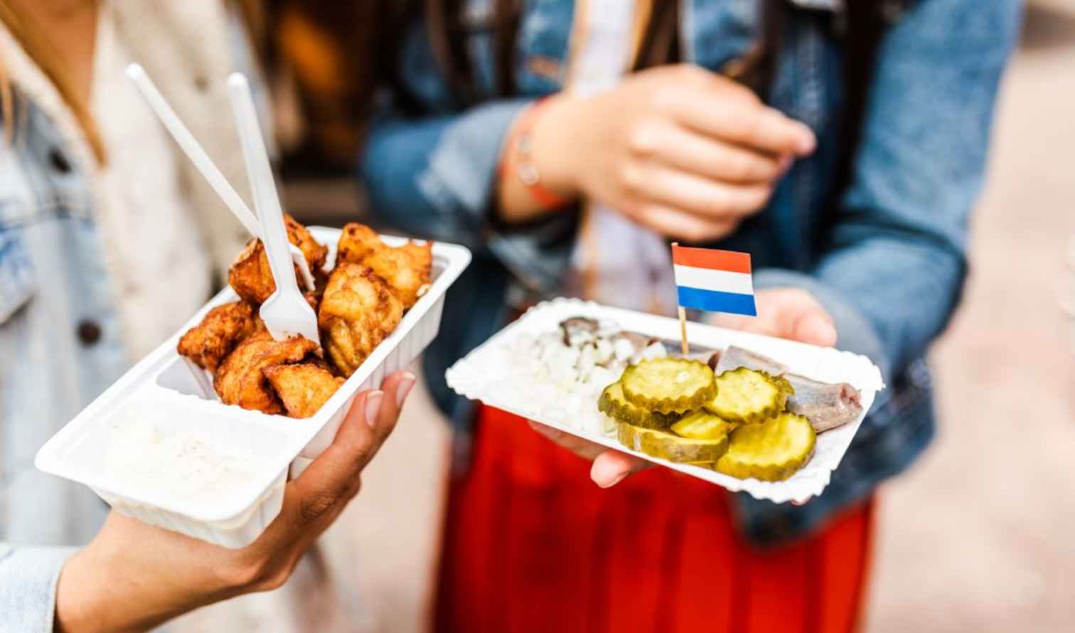 Two people holding Dutch street food with pickles and a flag in Amsterdam.