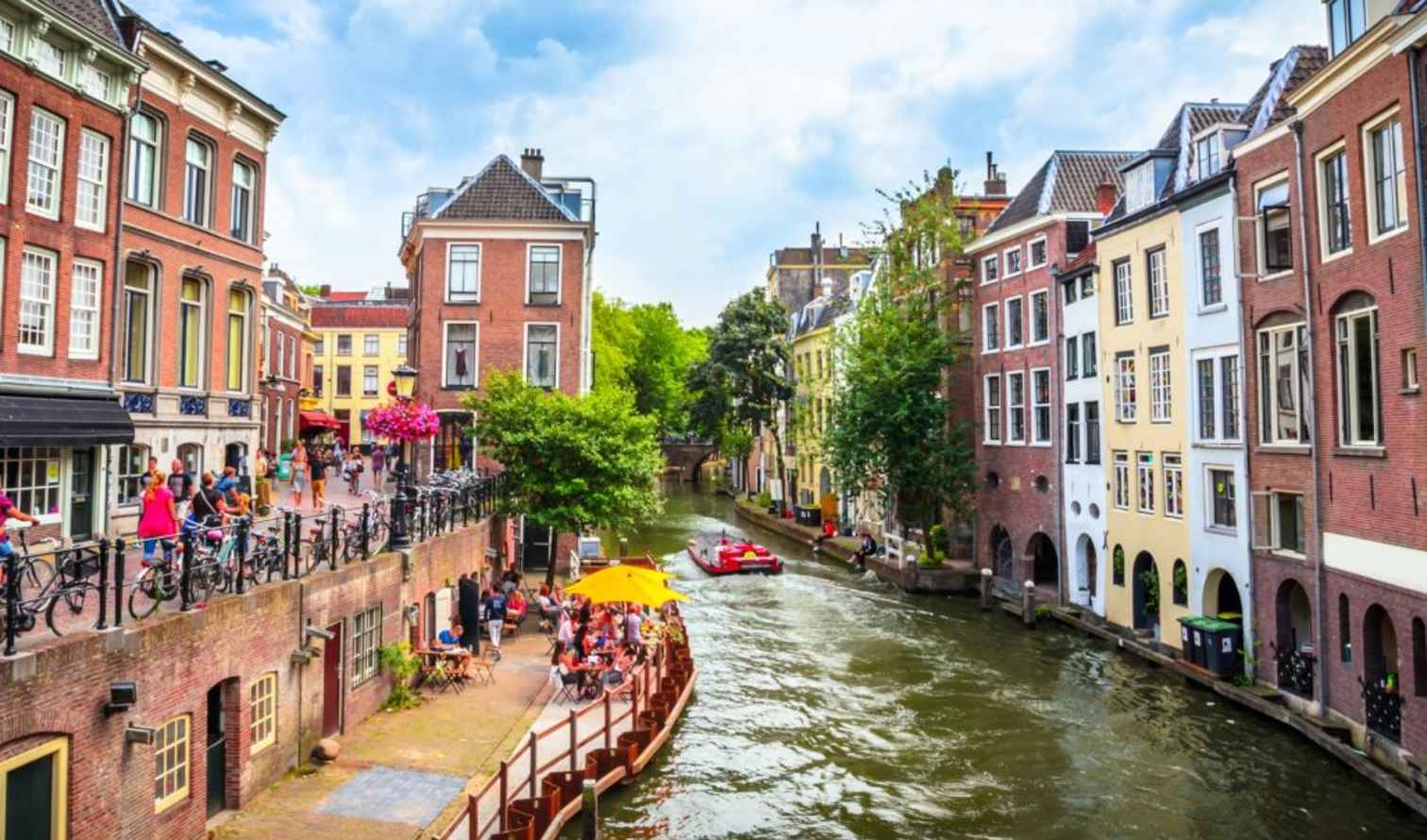 Pedestrian and cyclists on Oudegracht canal, Utrecht with outdoor seating visible.