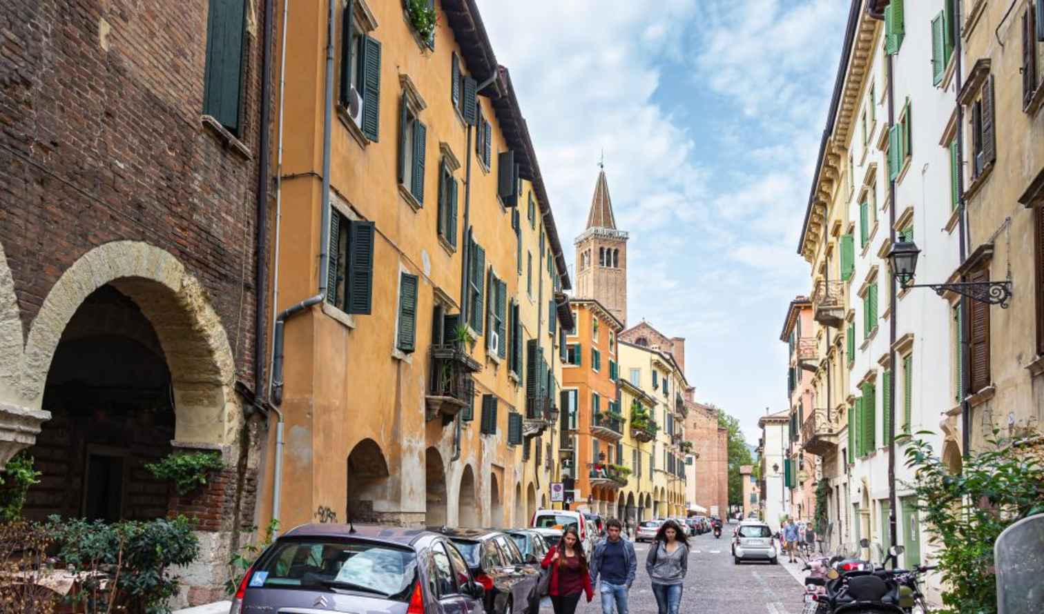 People walking along a narrow street with cars parked in Verona.