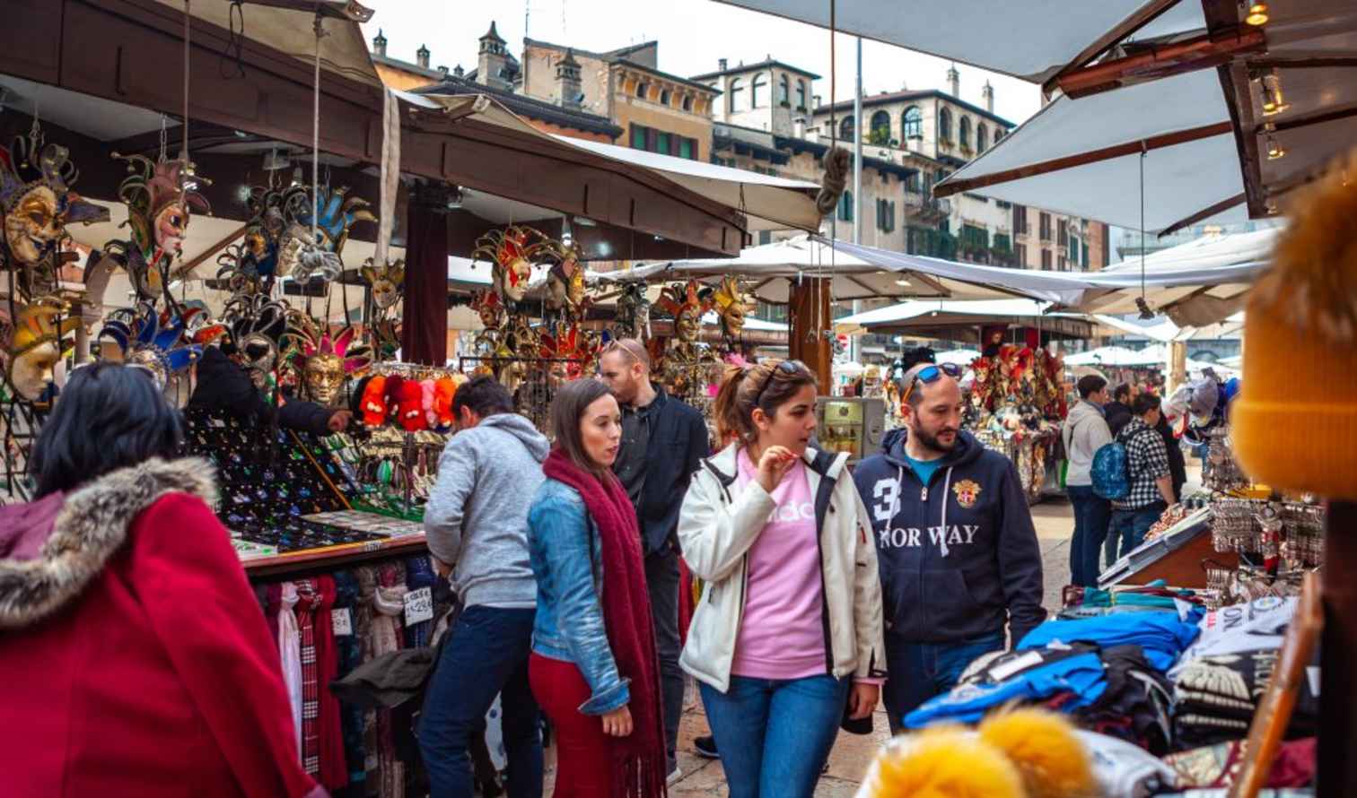 People browsing stalls at Piazza delle Erbe market in Verona, Italy.