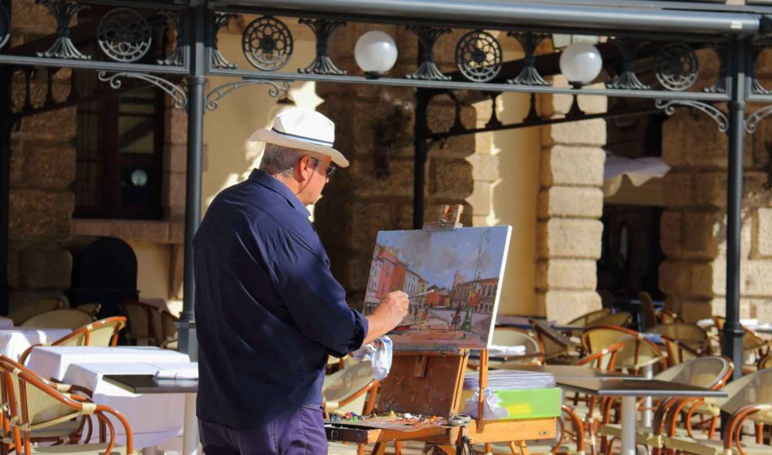 Artist painting outdoors at a cafe with arched stone columns in the background in Verona.