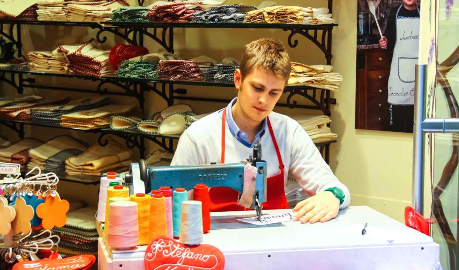 A young man sewing inside a fabric shop in Verona