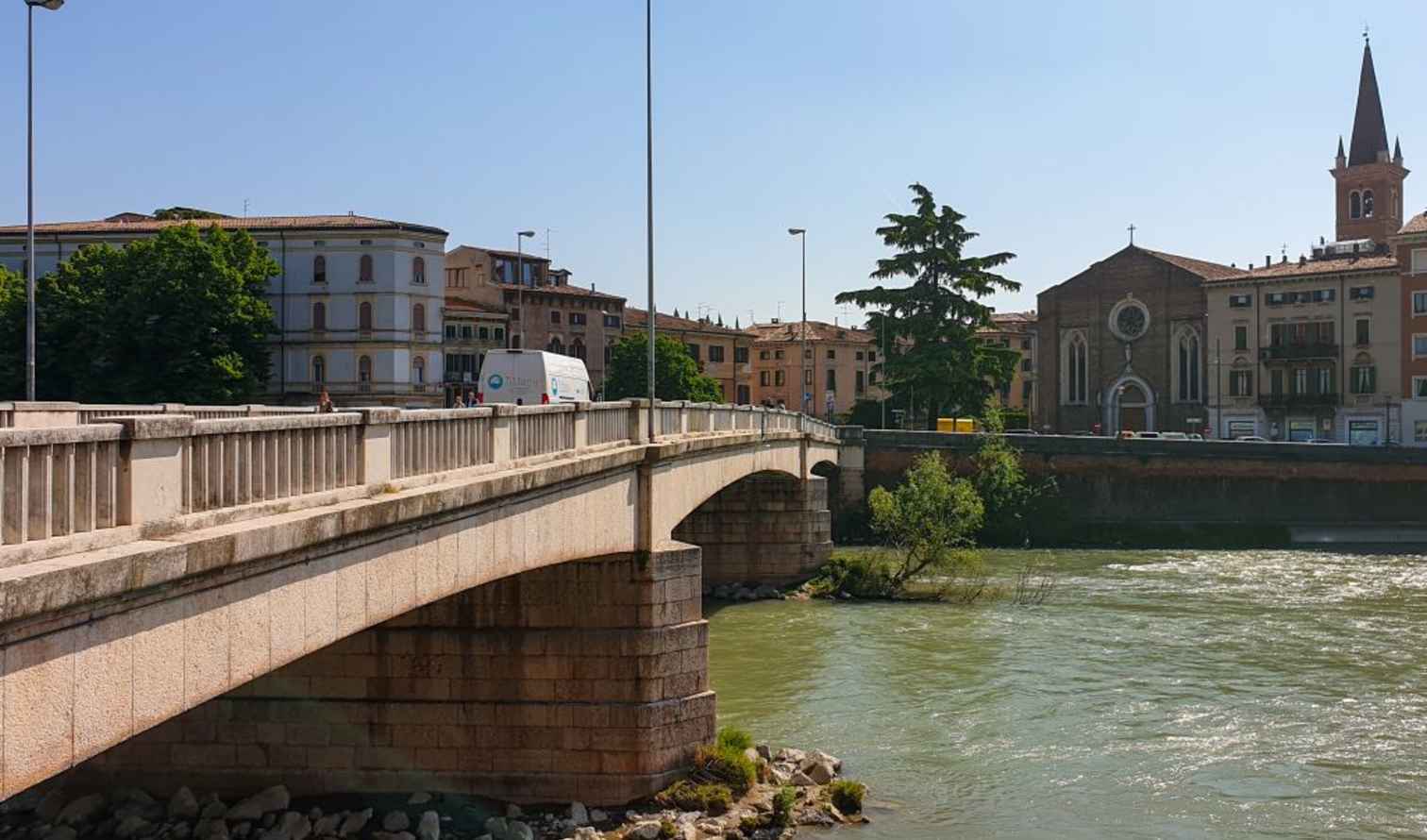 Street traffic crossing Ponte della Vittoria beside a church in Verona.