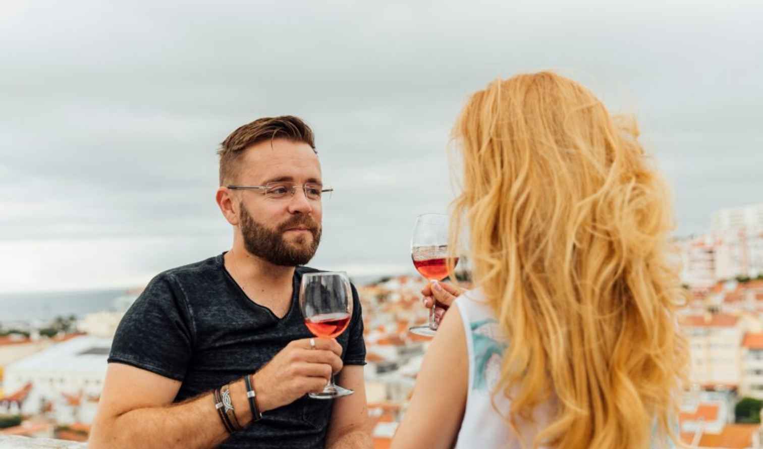 Two people hold wine glasses on a rooftop in Pisa, overlooking the city.