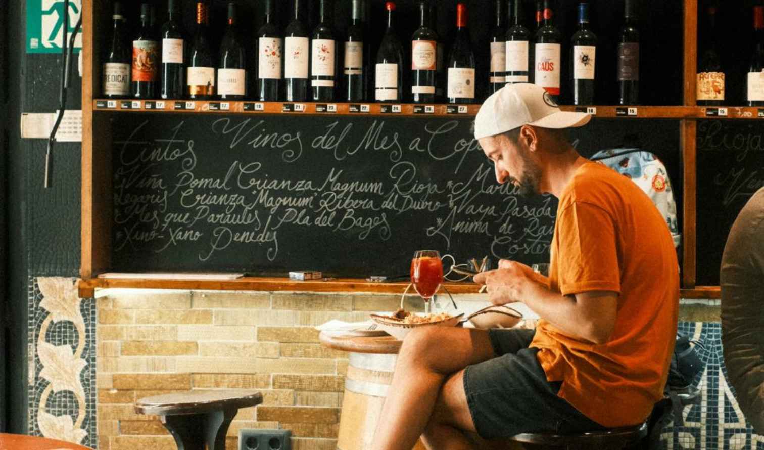 Man dining at a wine bar with bottles displayed overhead in Pisa.