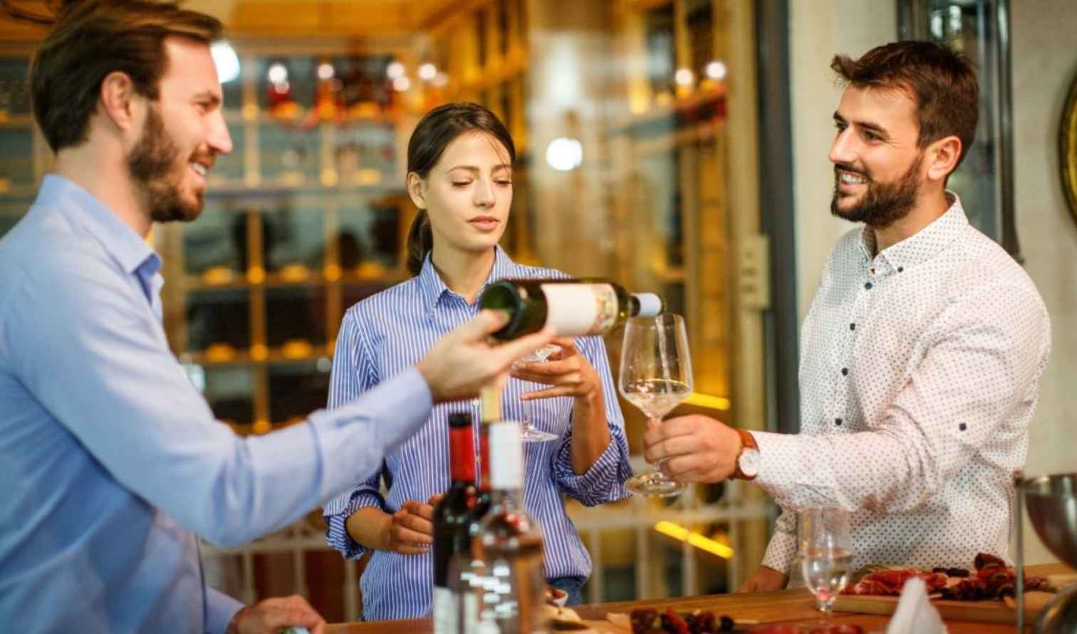 Two men and a woman at a bar counter with wine and glasses in Pisa.