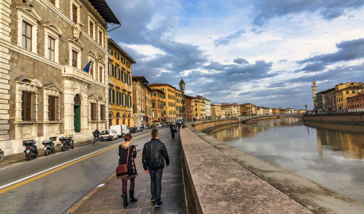 People walking along the Arno River in Pisa, Italy.