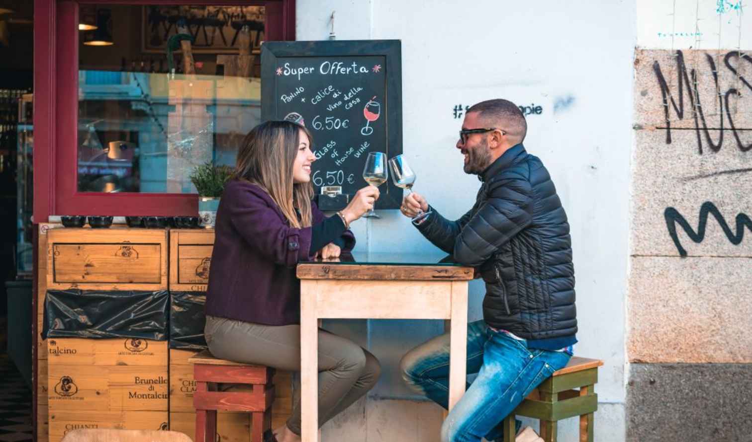 Two people sitting at an outdoor café table clinking glasses in Sienna