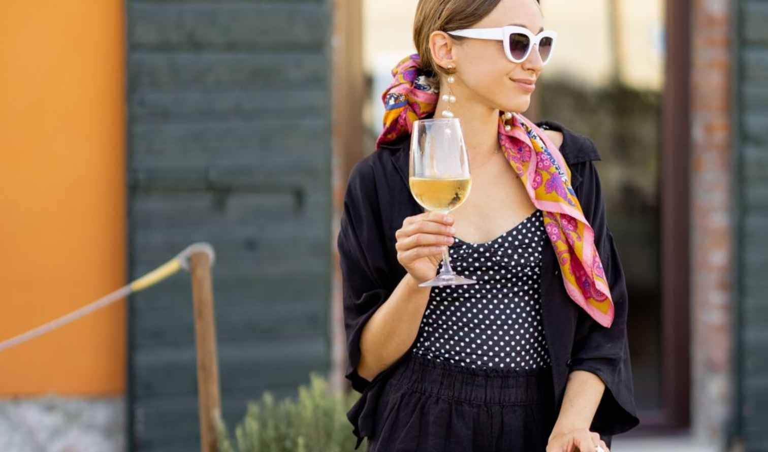 A woman holding a wine glass stands near a green wall in Sienna