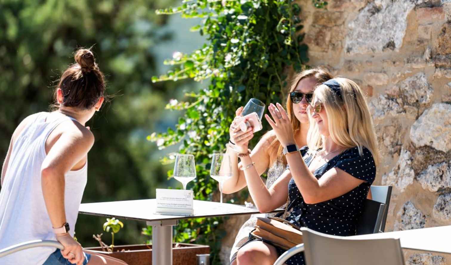 Three women seated at a table outdoors next to a stone wall in Sienna