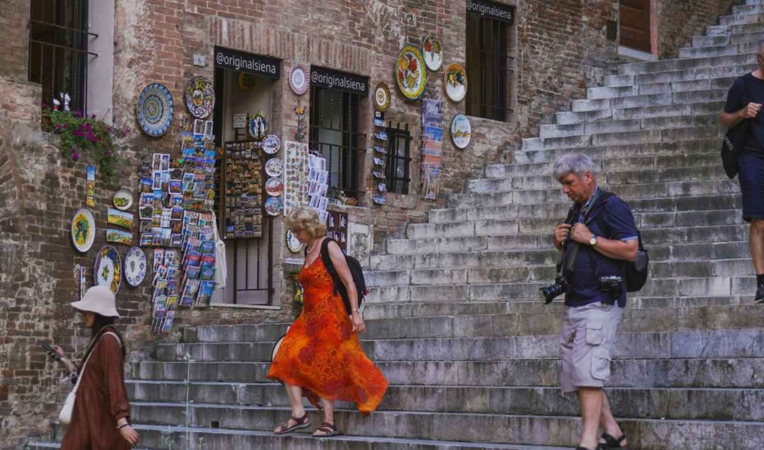People walking down stone steps in Siena, Italy, near a souvenir shop.