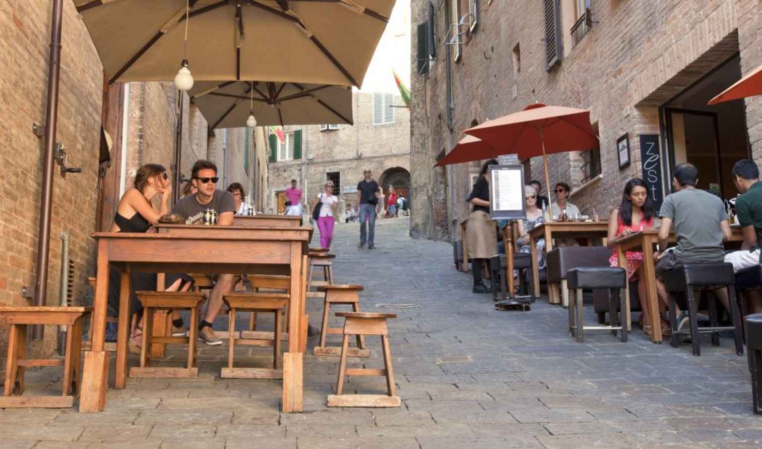 Outdoor dining on a narrow cobblestone street in Siena, Italy.