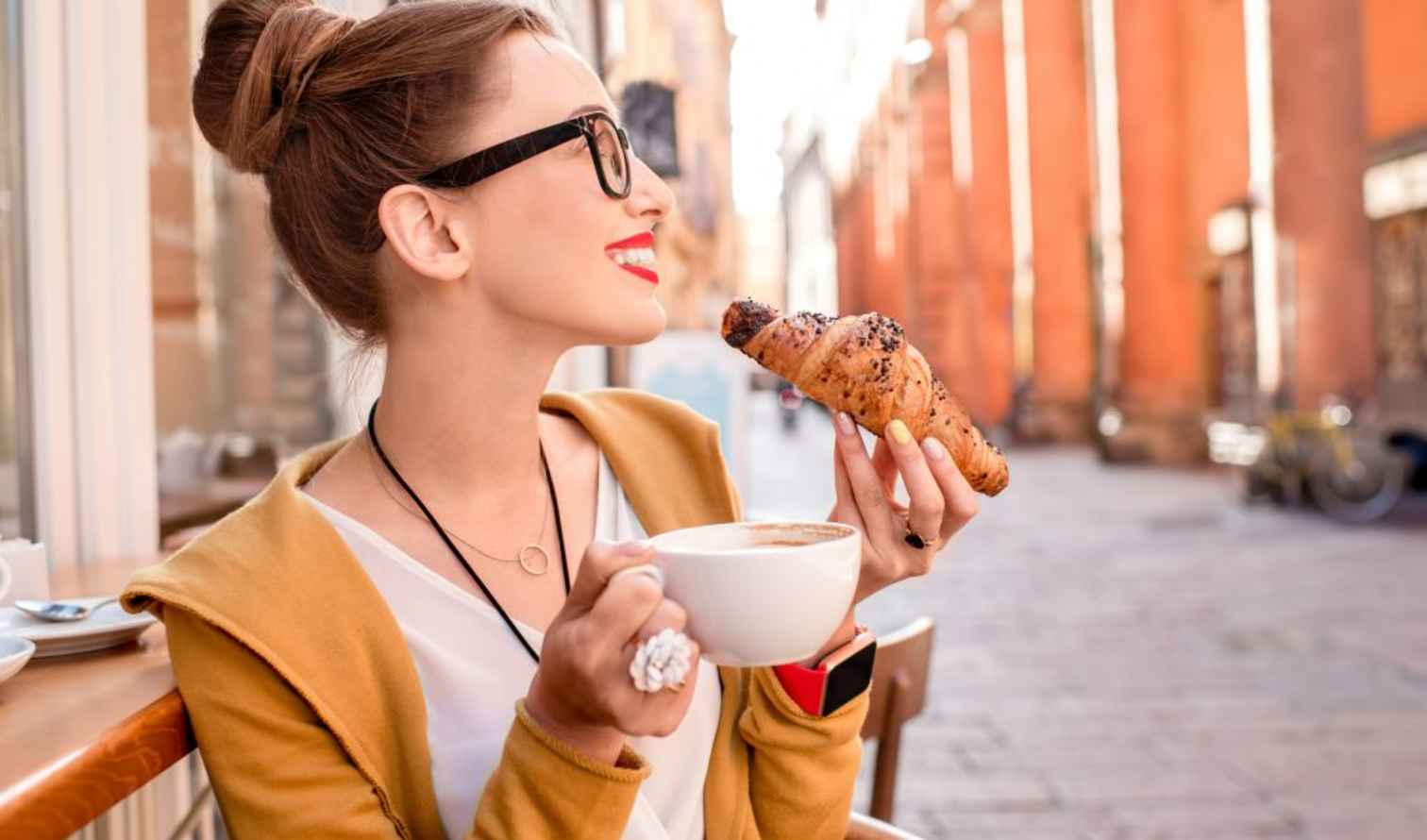 Woman eating a croissant and drinking coffee on a street in Siena