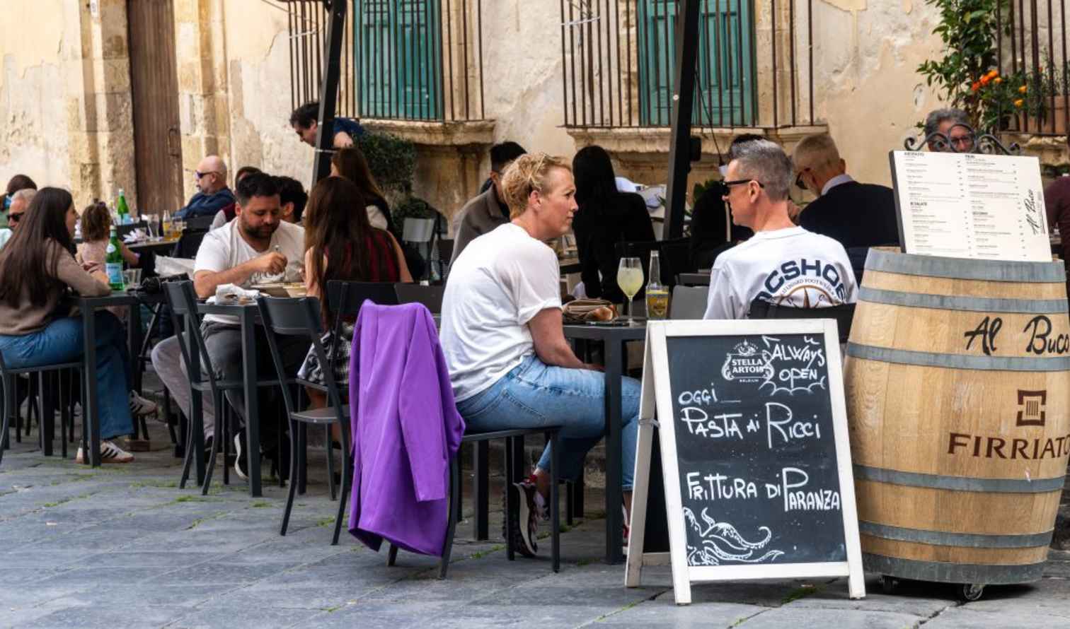 People sitting at tables with menus and barrels outside a Sicilian café in Verona