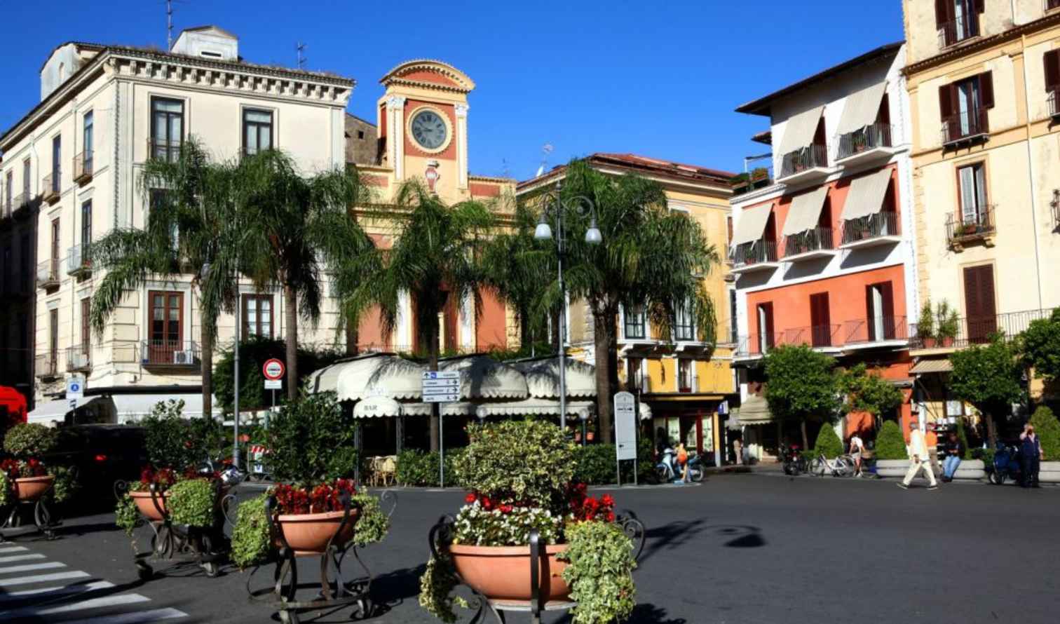 People walking by buildings and palm trees in Sorrento, Italy.