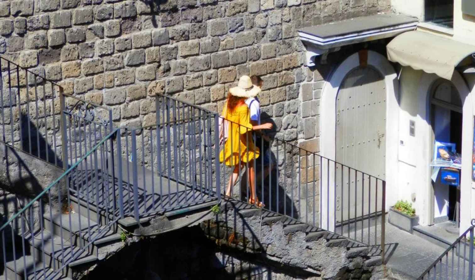 Two people walking up a stone staircase beside a brick wall in Sorrento