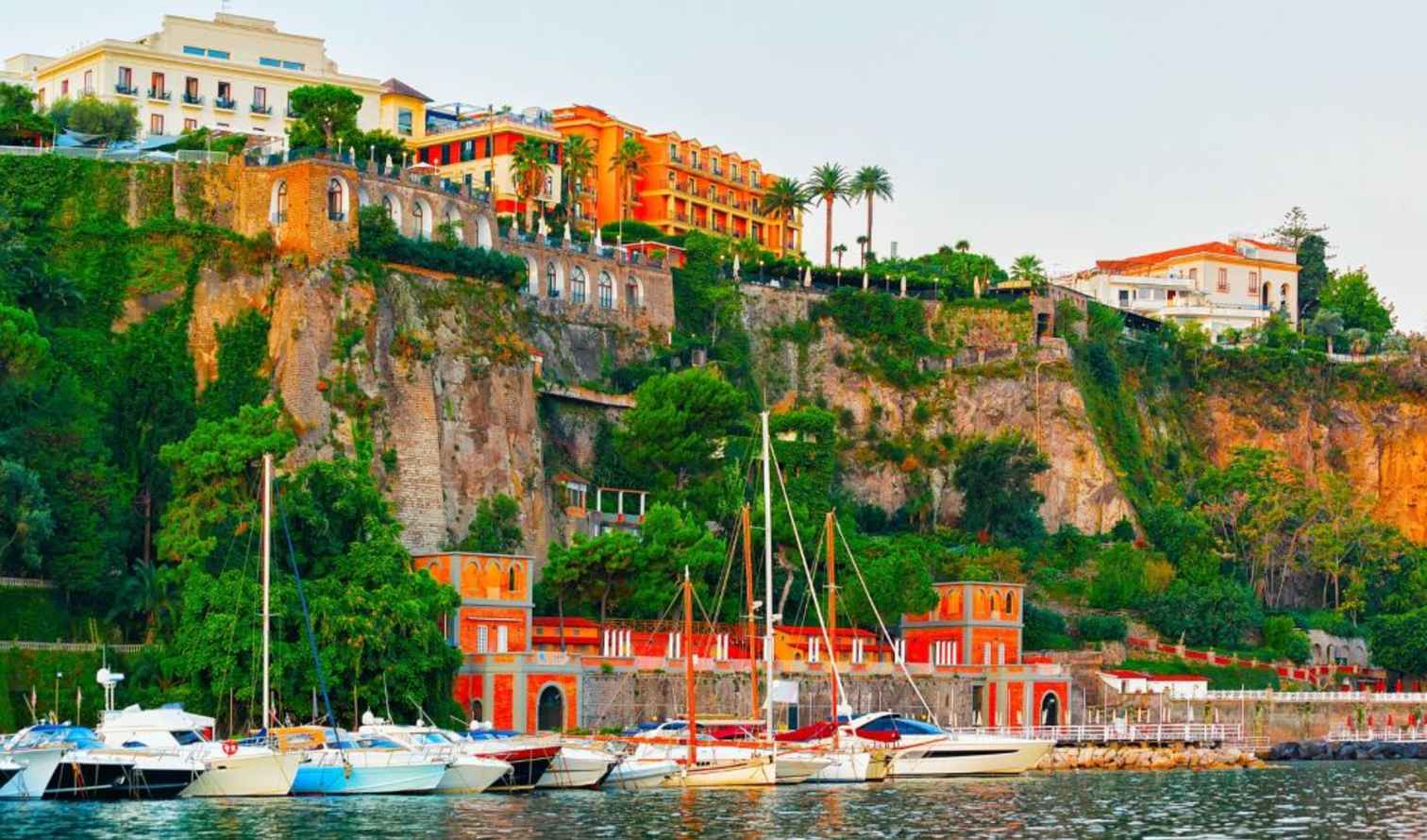 Boats docked at the Marina Piccola in Sorrento, Italy, with cliffside buildings.