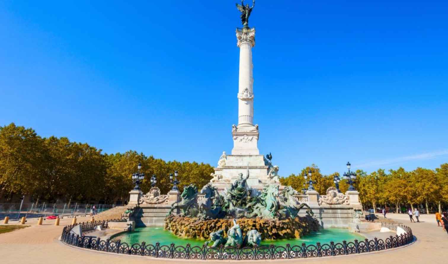 Place des Quinconces fountain with monument in Bordeaux under clear blue sky.