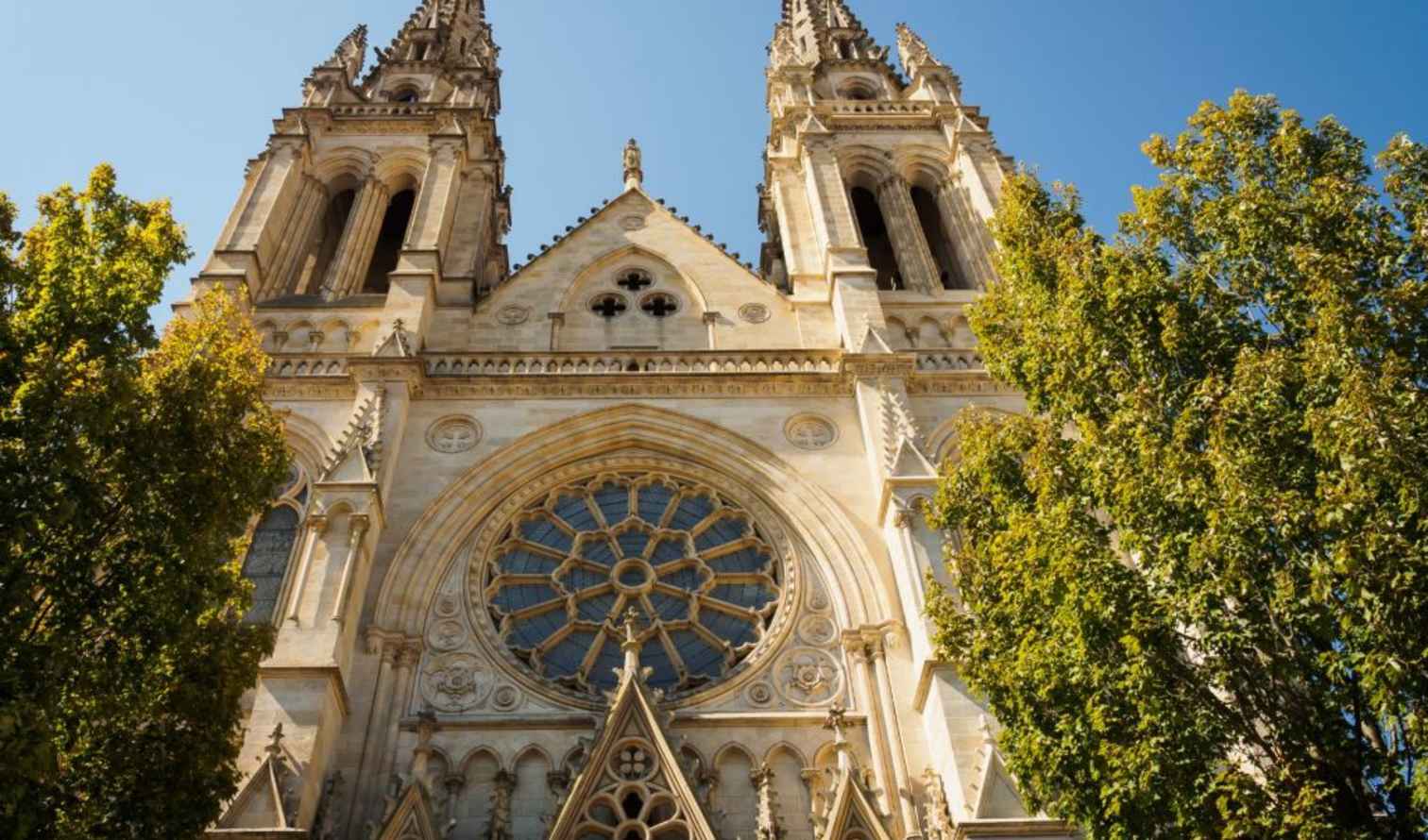 Gothic-style cathedral towers rise between two trees in Bordeaux.