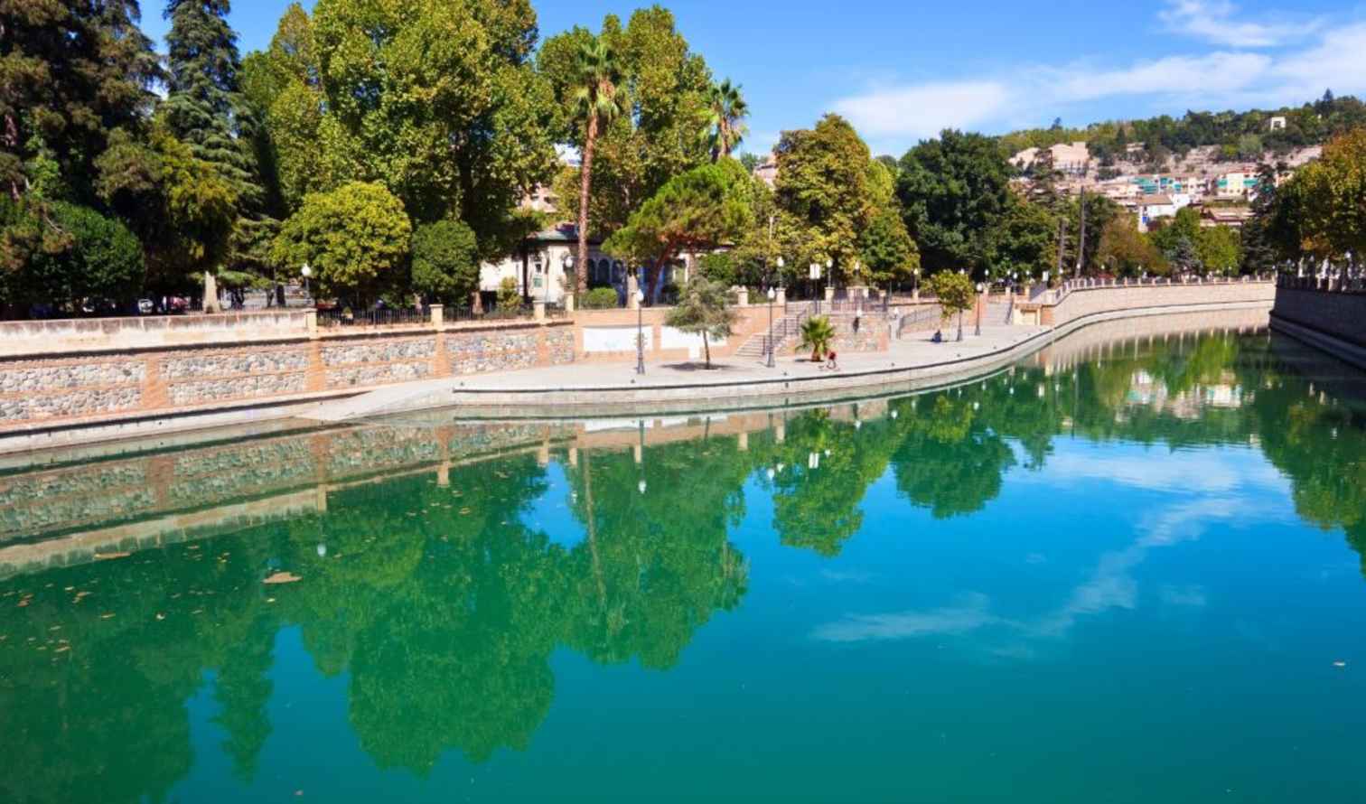 River lined with trees and stone wall, possibly in a Mediterranean city in Granada