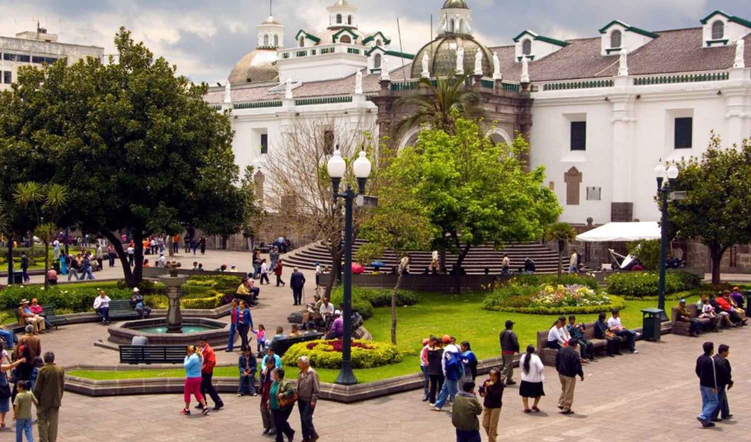 People walking and sitting in Plaza Grande, Quito, with the white cathedral in background.