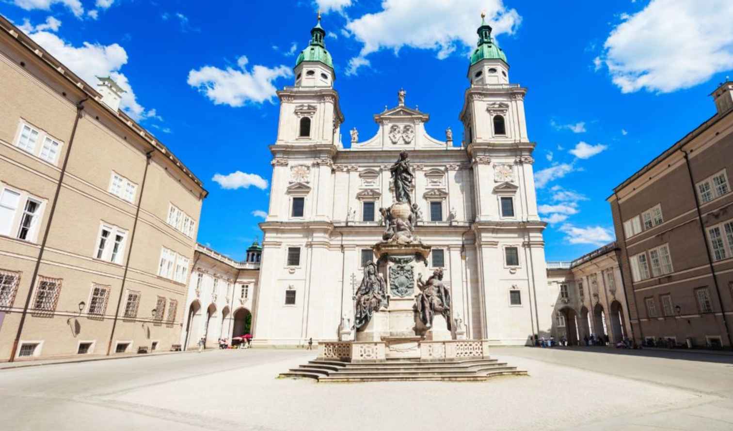 Twin green towers of Salzburg Cathedral under a blue sky.