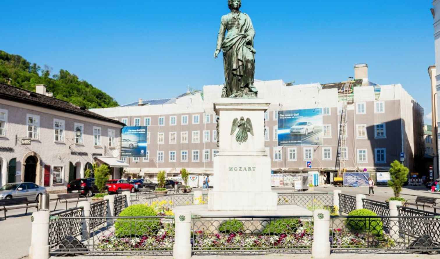 Mozart statue in Mozartplatz, Salzburg with surrounding buildings and parked cars.