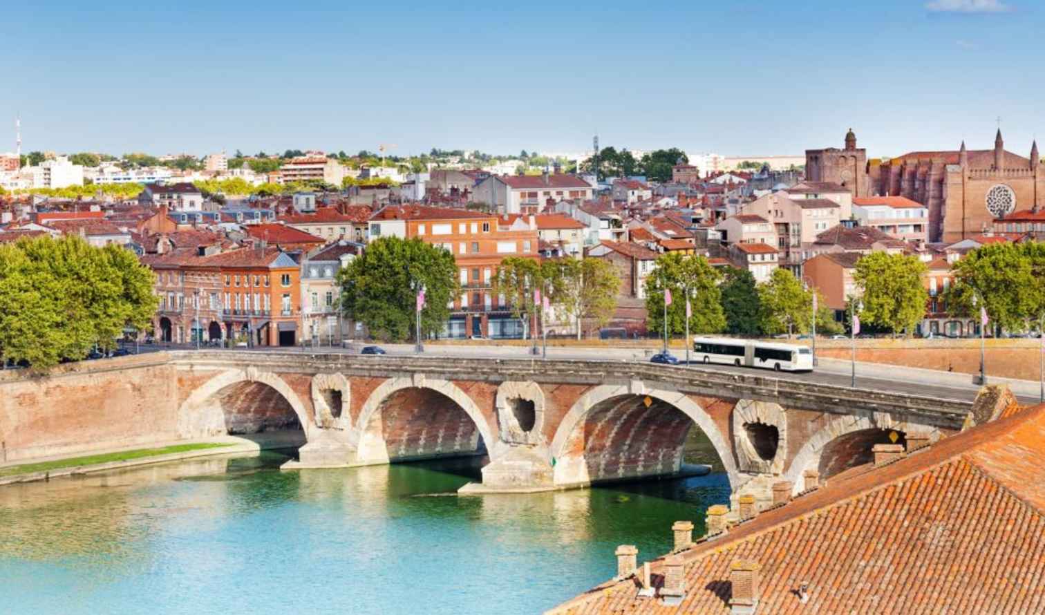 Pont Neuf bridge over the Garonne River in Toulouse, France, with city buildings in background.