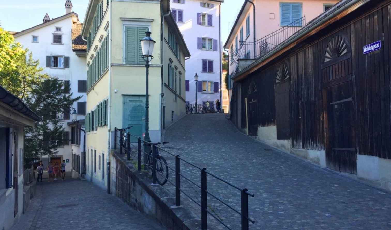 Narrow cobblestone street in Zurich with people walking and bicycles parked.