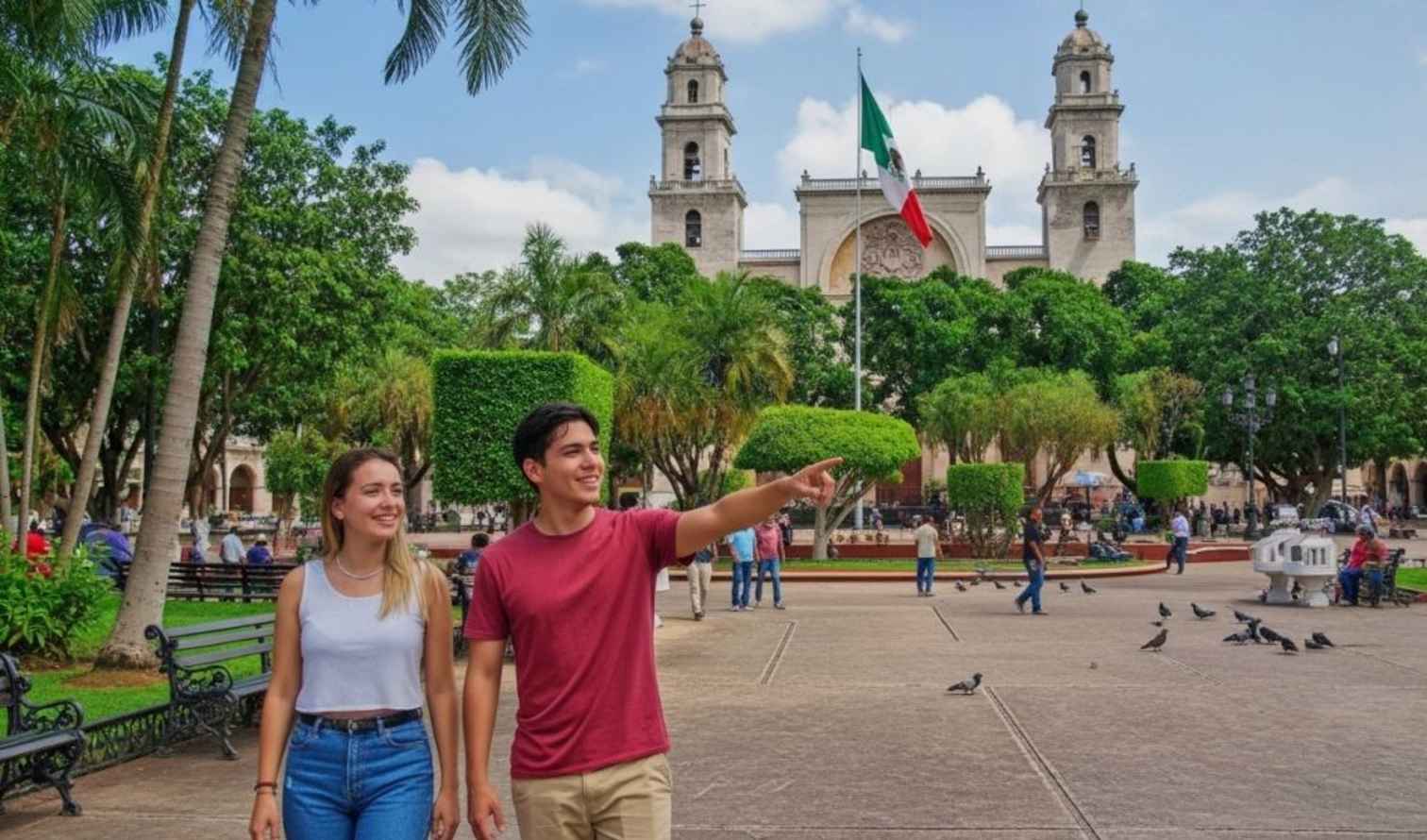 Two people walk in Plaza Grande, Mérida, with pigeons nearby.