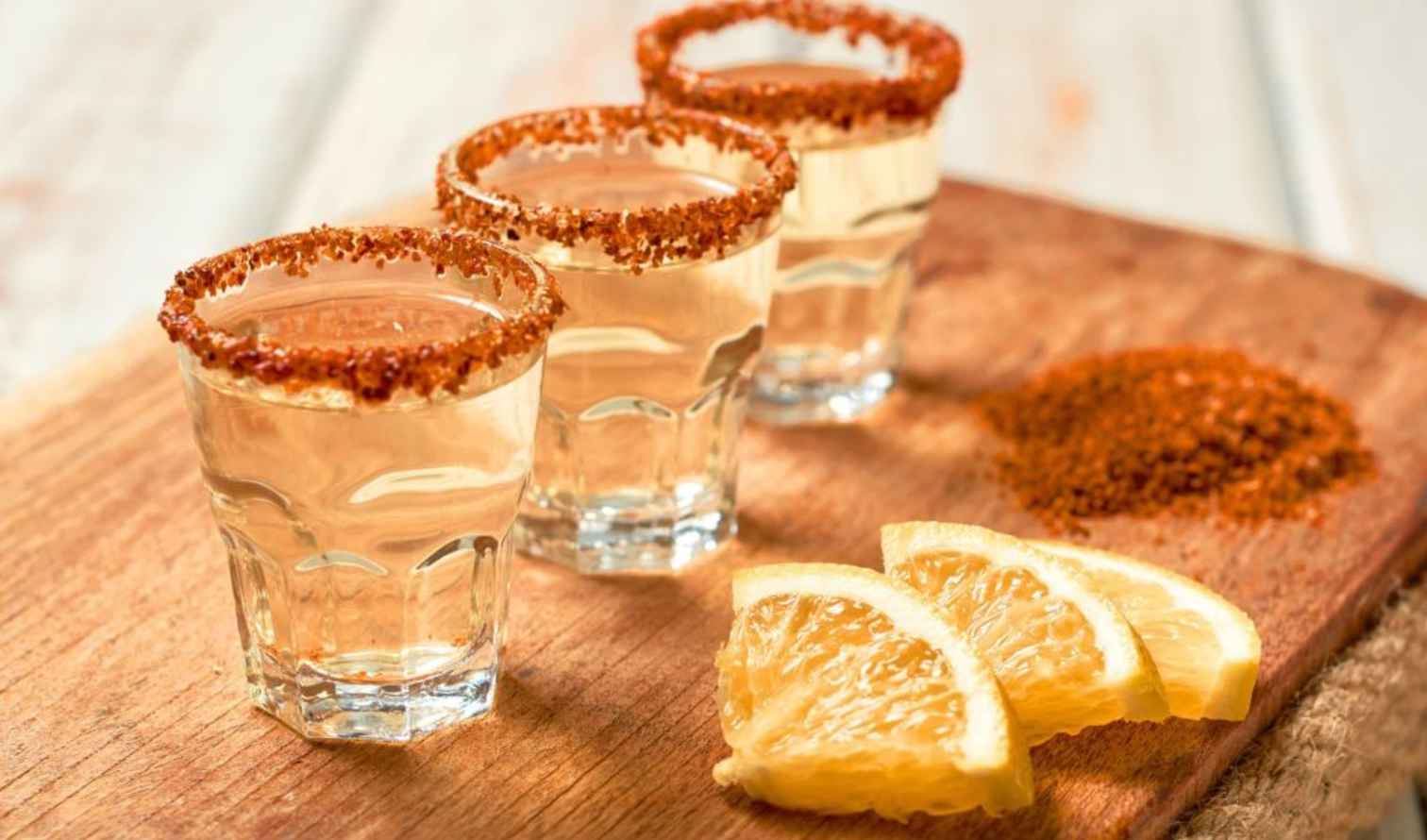 Three shot glasses with chili salt rims on a wooden board in Oaxaca