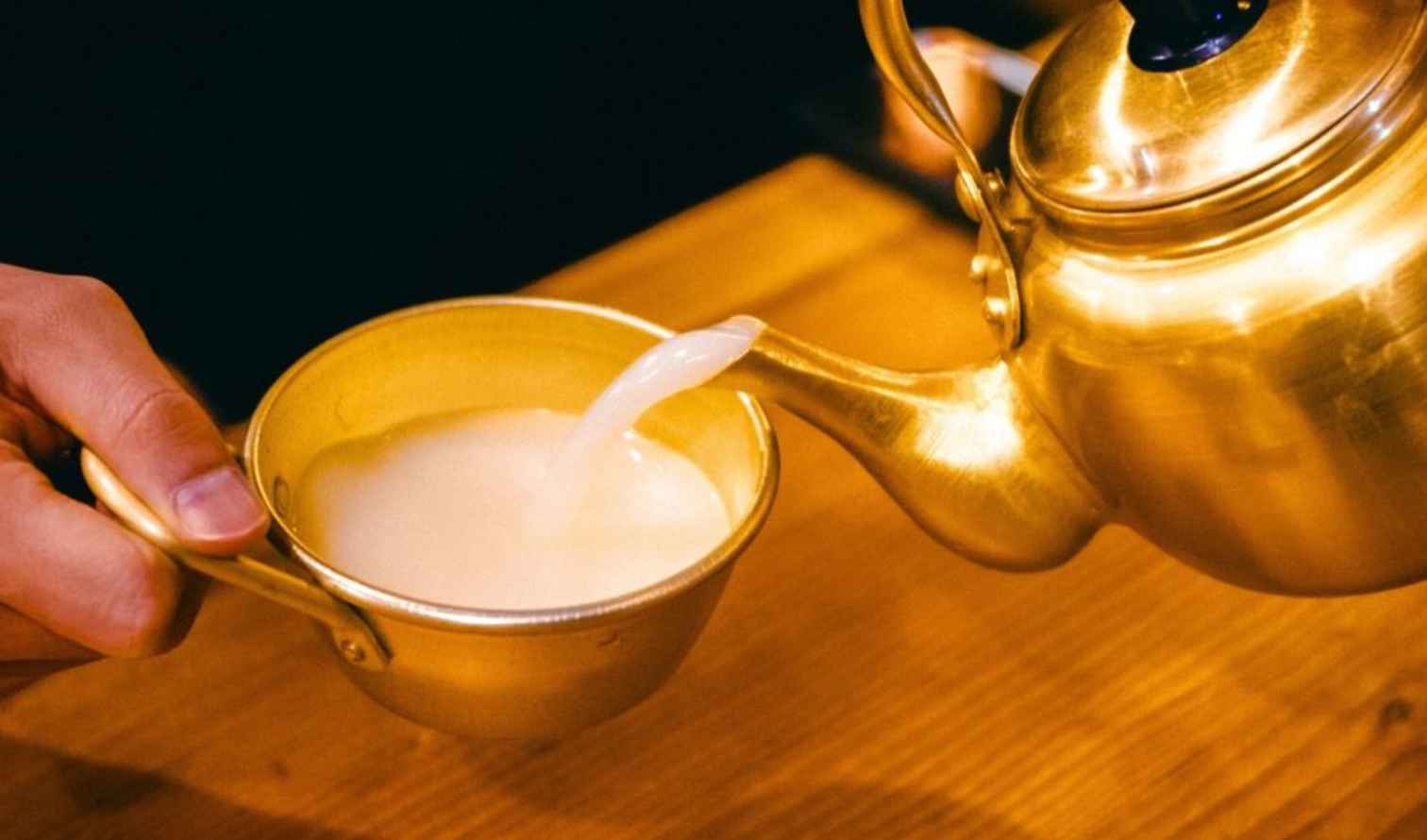 Hand pouring liquid from a brass kettle into a matching brass cup in Busan