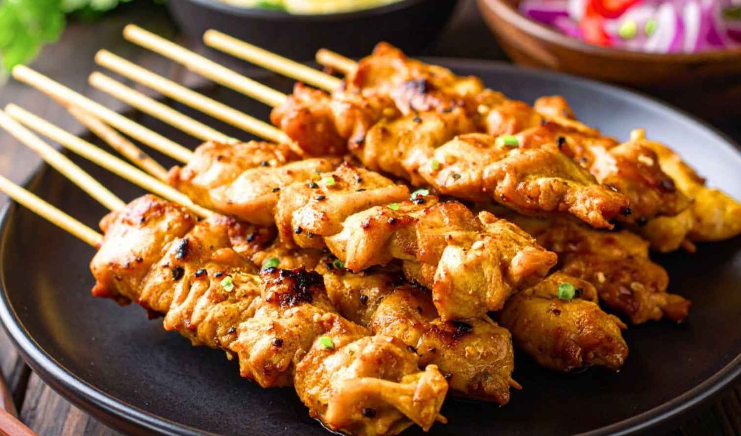 Grilled chicken skewers on a black plate with garnishing in Perth.