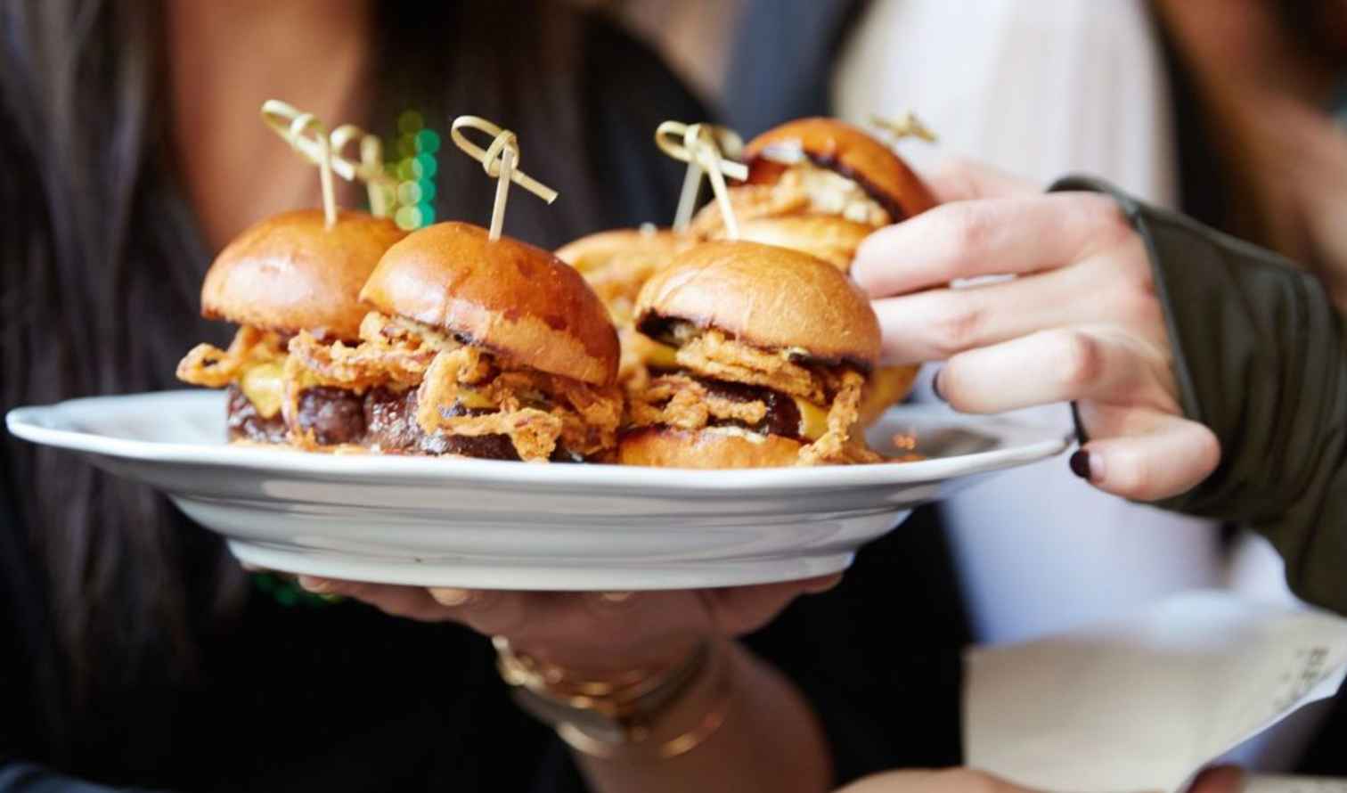 Close-up of mini burgers on a white plate held by someone in Brisbane