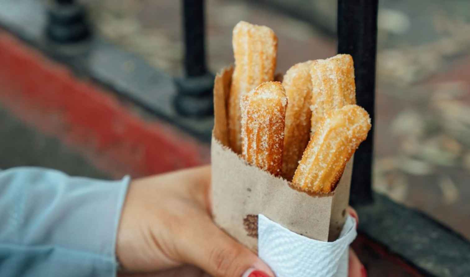 A hand holding a paper bag of churros near a metal railing in Guadalajara.