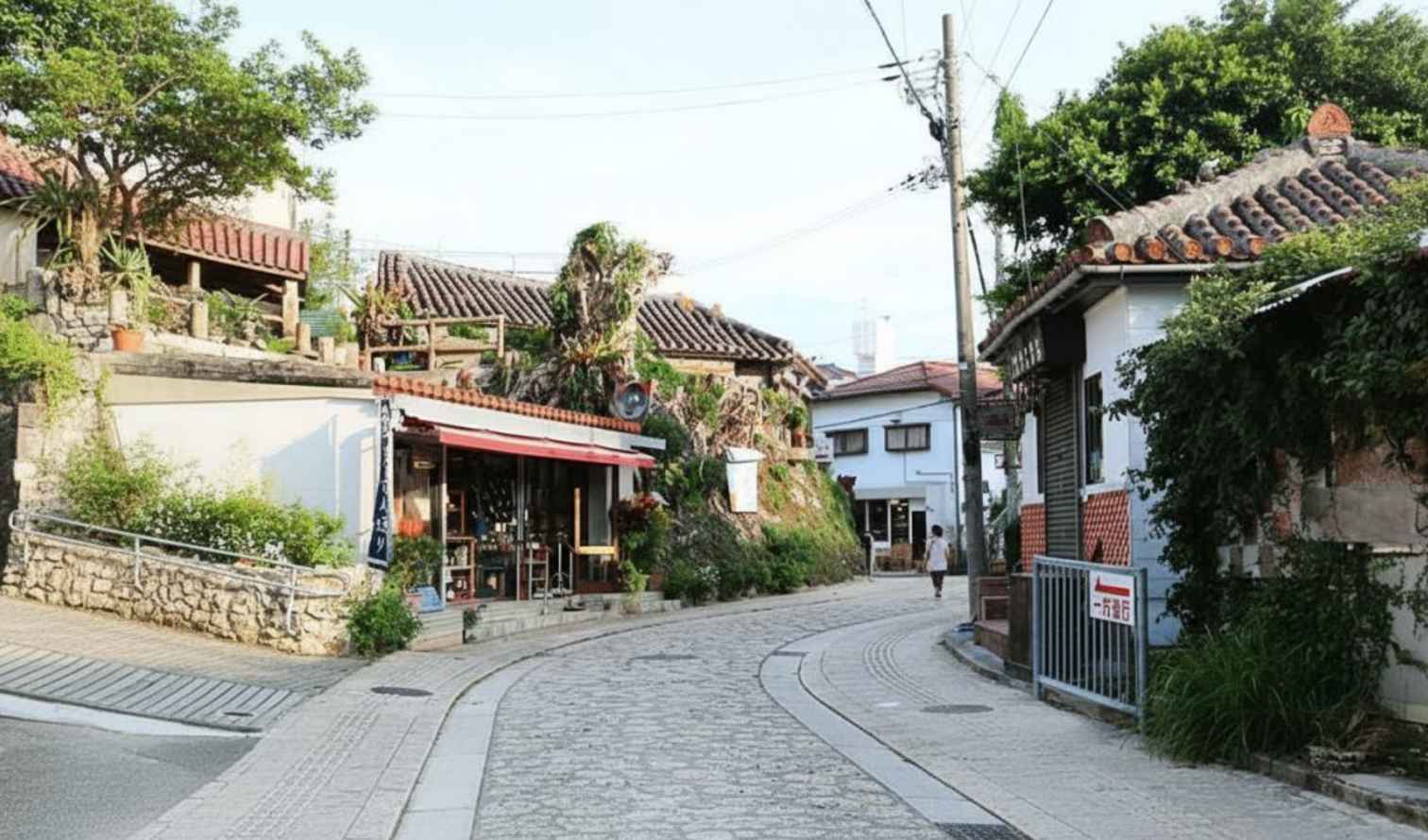 Tiled-roof buildings line a narrow, stone-paved street in Naha, Japan.