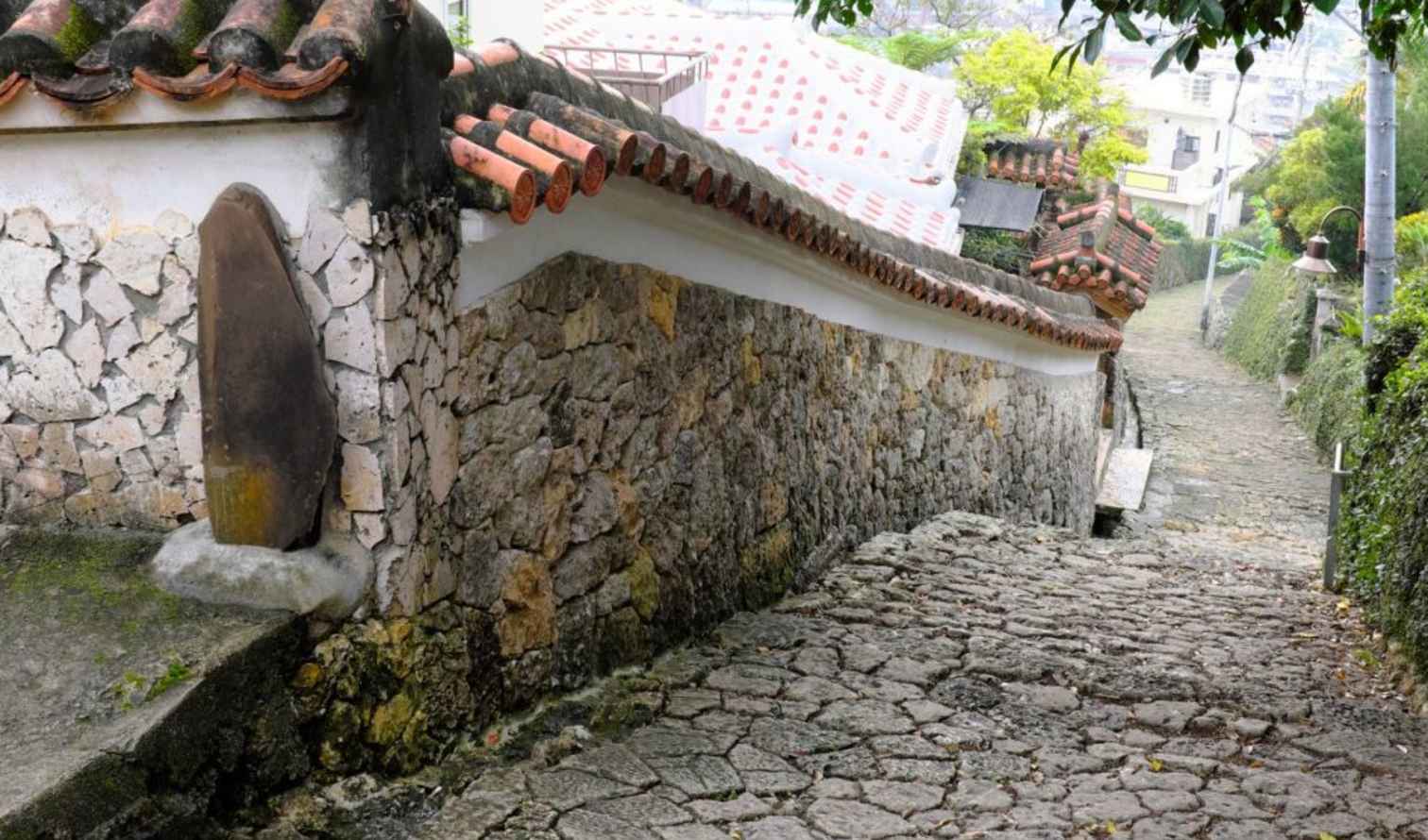 Stone pathway with traditional Ryukyu architecture and red-tiled roof in Naha, Okinawa.