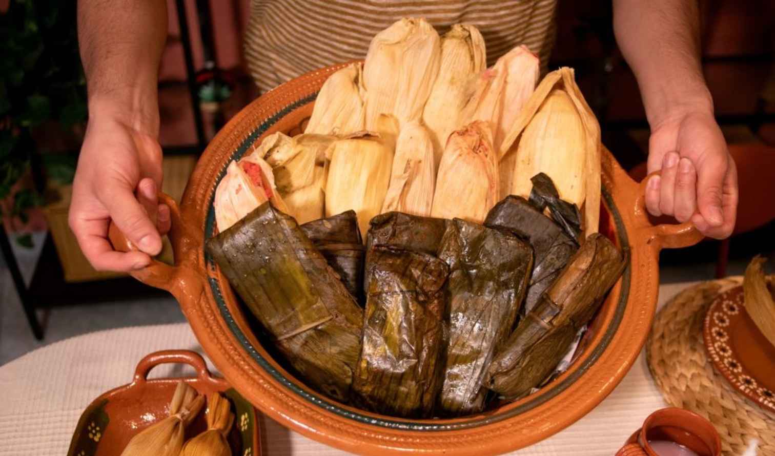 A person holding a platter of tamales wrapped in corn husks and banana leaves in Puebla