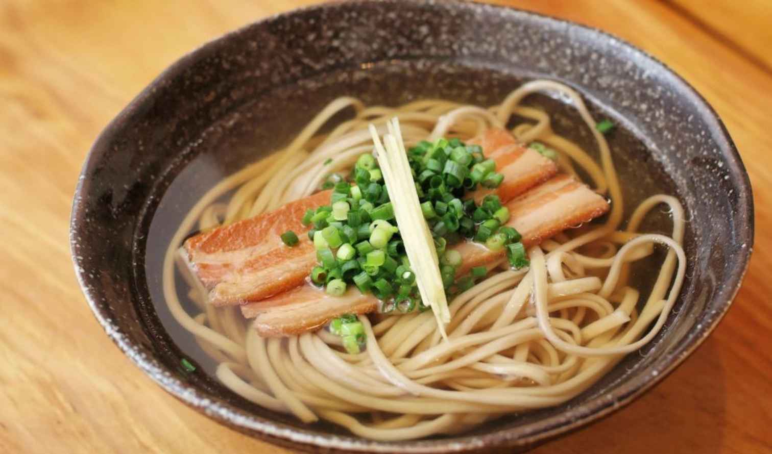 Bowl of Okinawa soba with pork and green onions on a wooden table in Naha