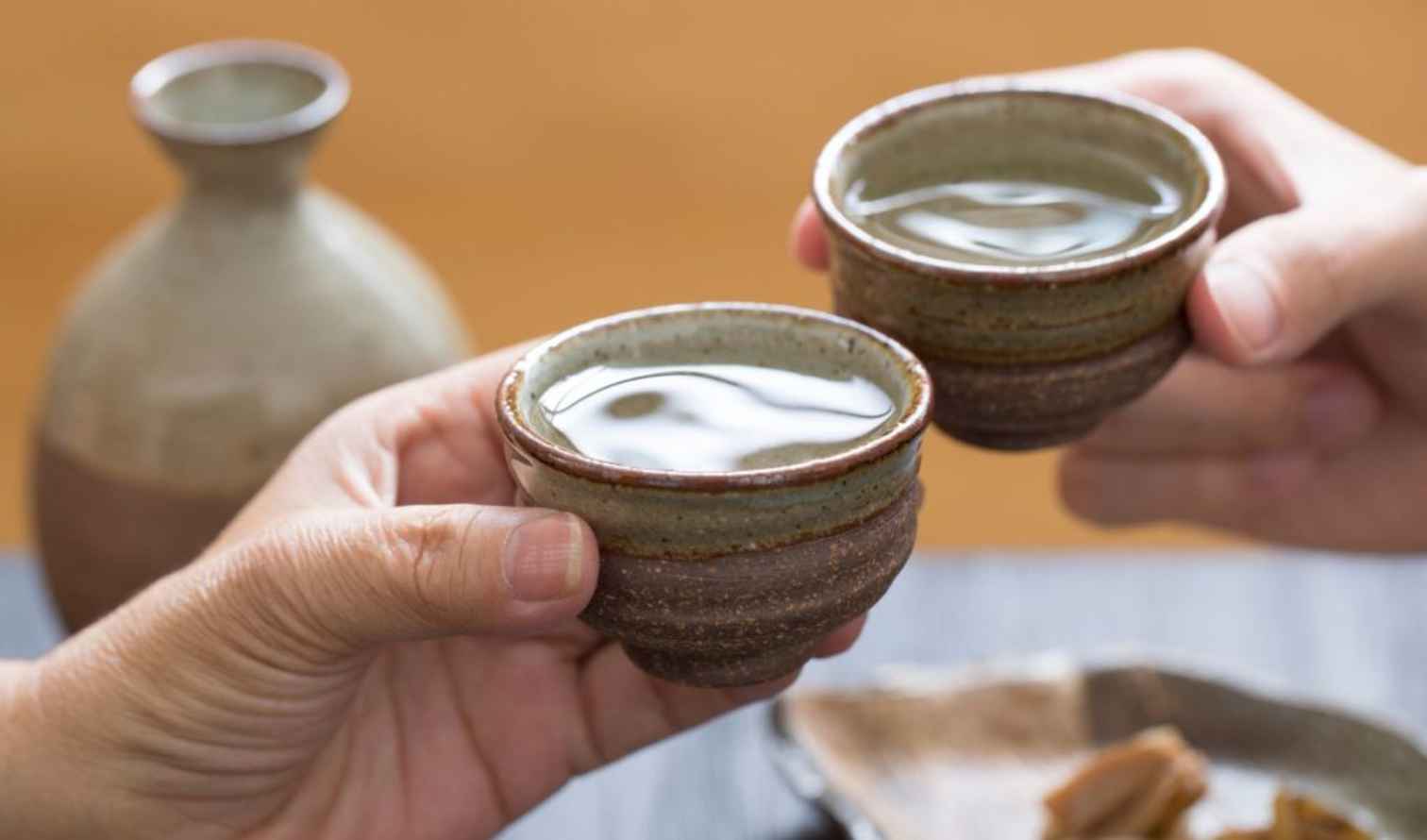 Two people holding ceramic sake cups in a toast in Nara